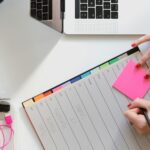 person holding pencil and stick note beside table